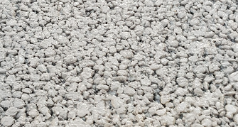 Detailaufnahme von grobkörnigem, frischem Beton. Die Oberfläche besteht aus vielen kleinen, unregelmäßig geformten Steinen, die dicht nebeneinanderliegen und eine raue, noch nicht ausgehärtete Struktur zeigen